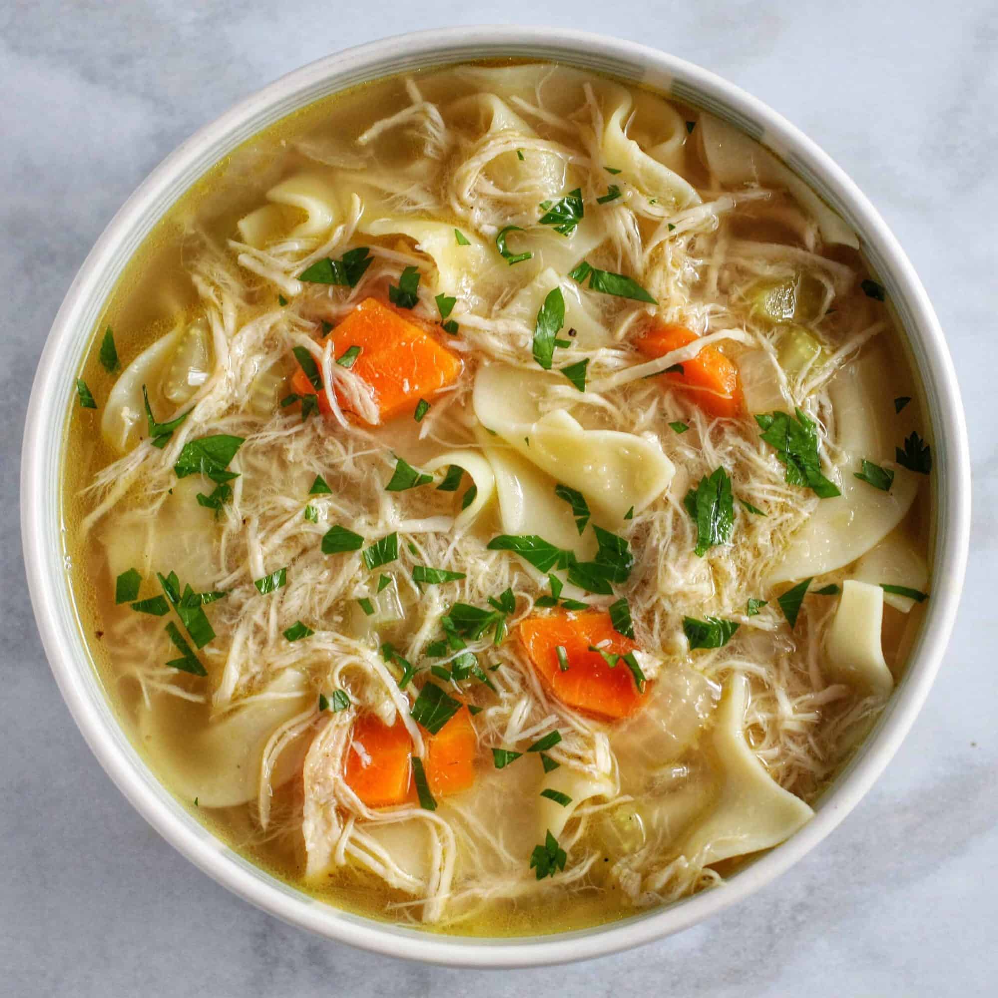 Overhead view of a bowl of homemade chicken noodle soup topped with chopped parsley.