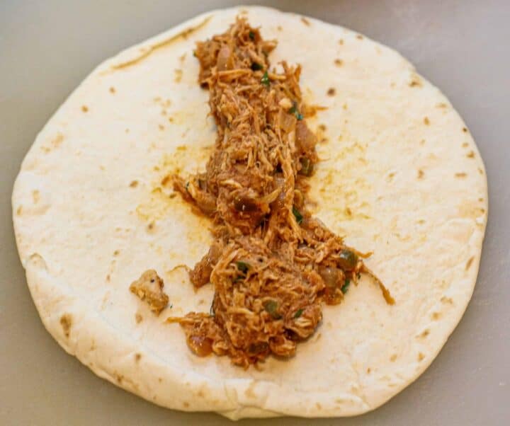 A tortilla with shredded chicken scooped onto the middle. 