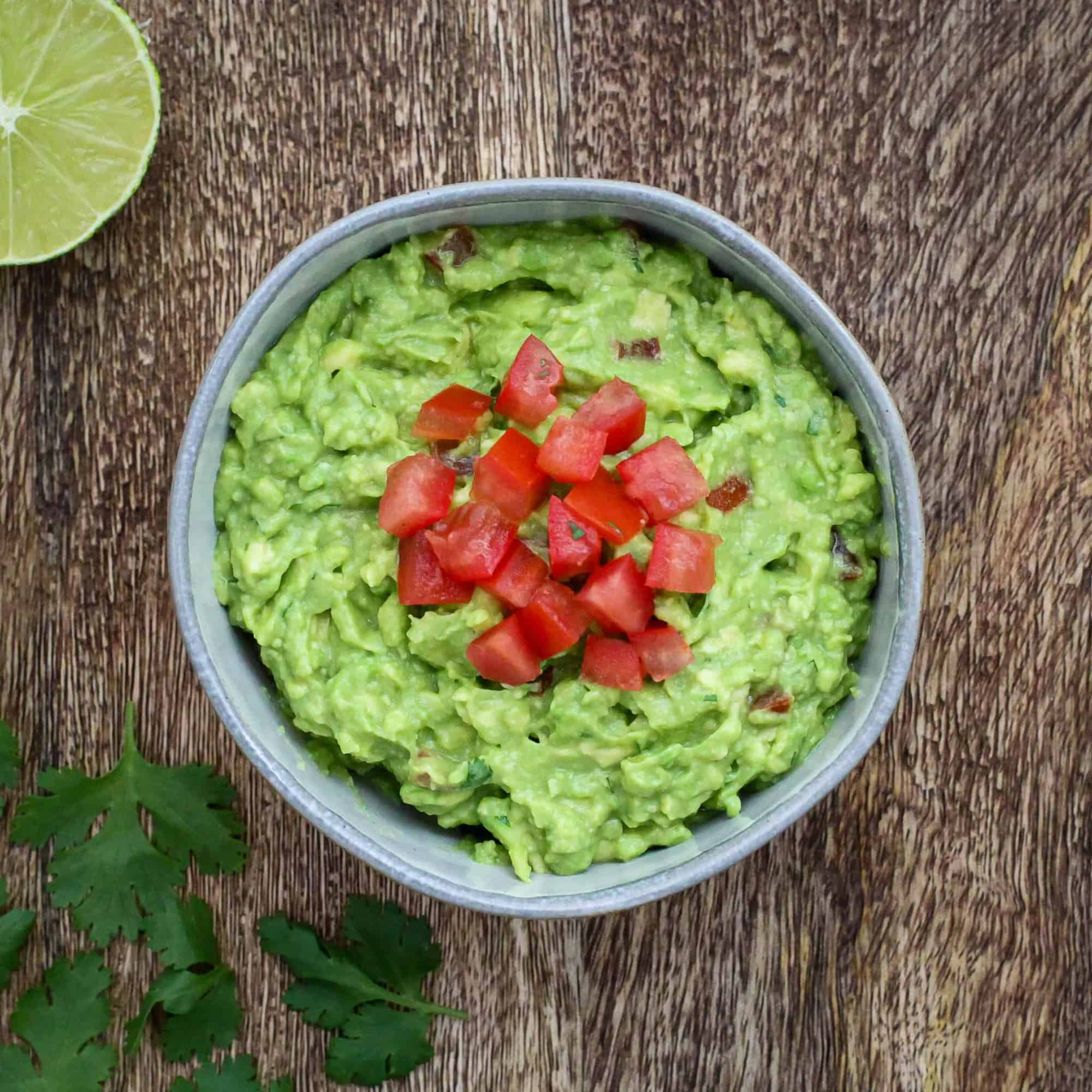 Homemade Guacamole ina serving bowl topped with diced tomatoes.