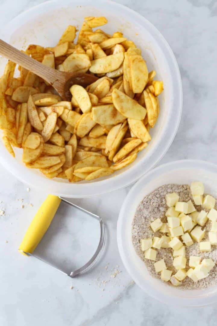 A bowl of seasoned sliced apples next to a bowl of the ingredients for the apple crisp topping.