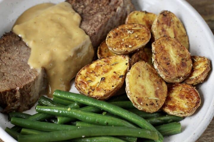 Crispy golden brown roasted potatoes on a plate with a slice of roast beef.