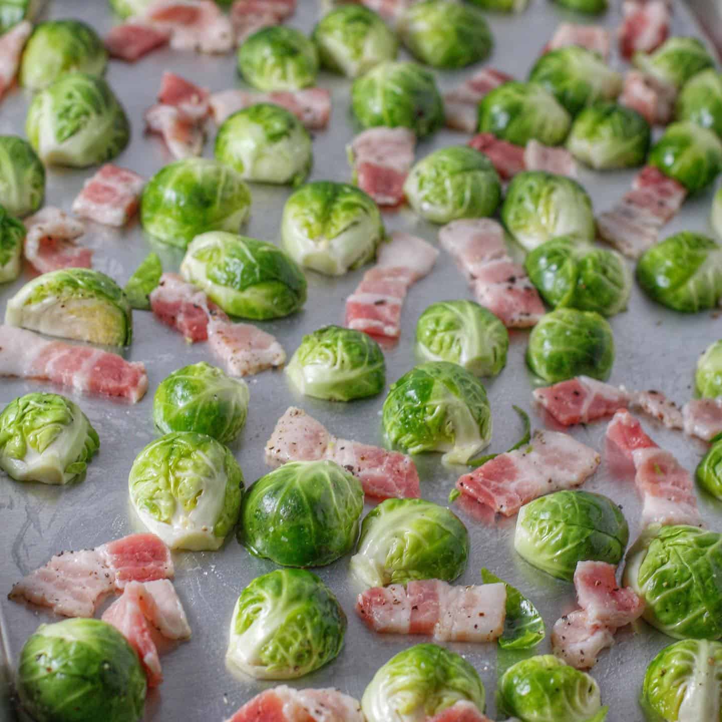 Brussels sprouts shown on a baking sheets with strips of bacon prior to roasting.