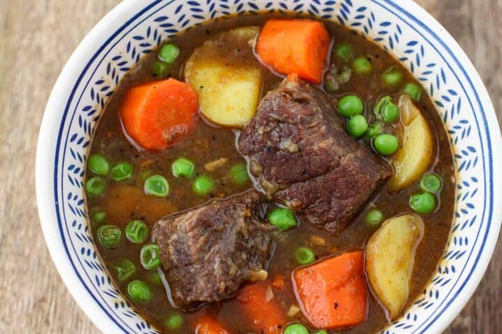 A bowl full of chunky beef stew with carrots, potatoes, and peas.