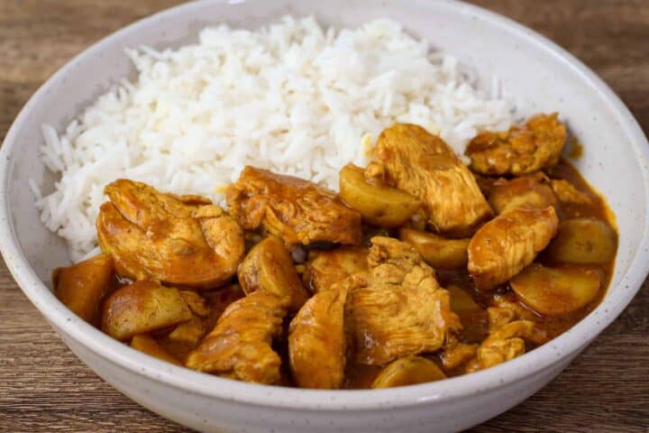 Side view of a plate of yellow curry chicken with potatoes served with steamed rice.