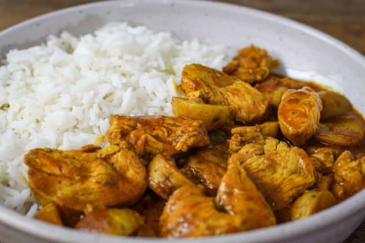 Side view of a serving of chicken curry with potatoes and steamed rice.