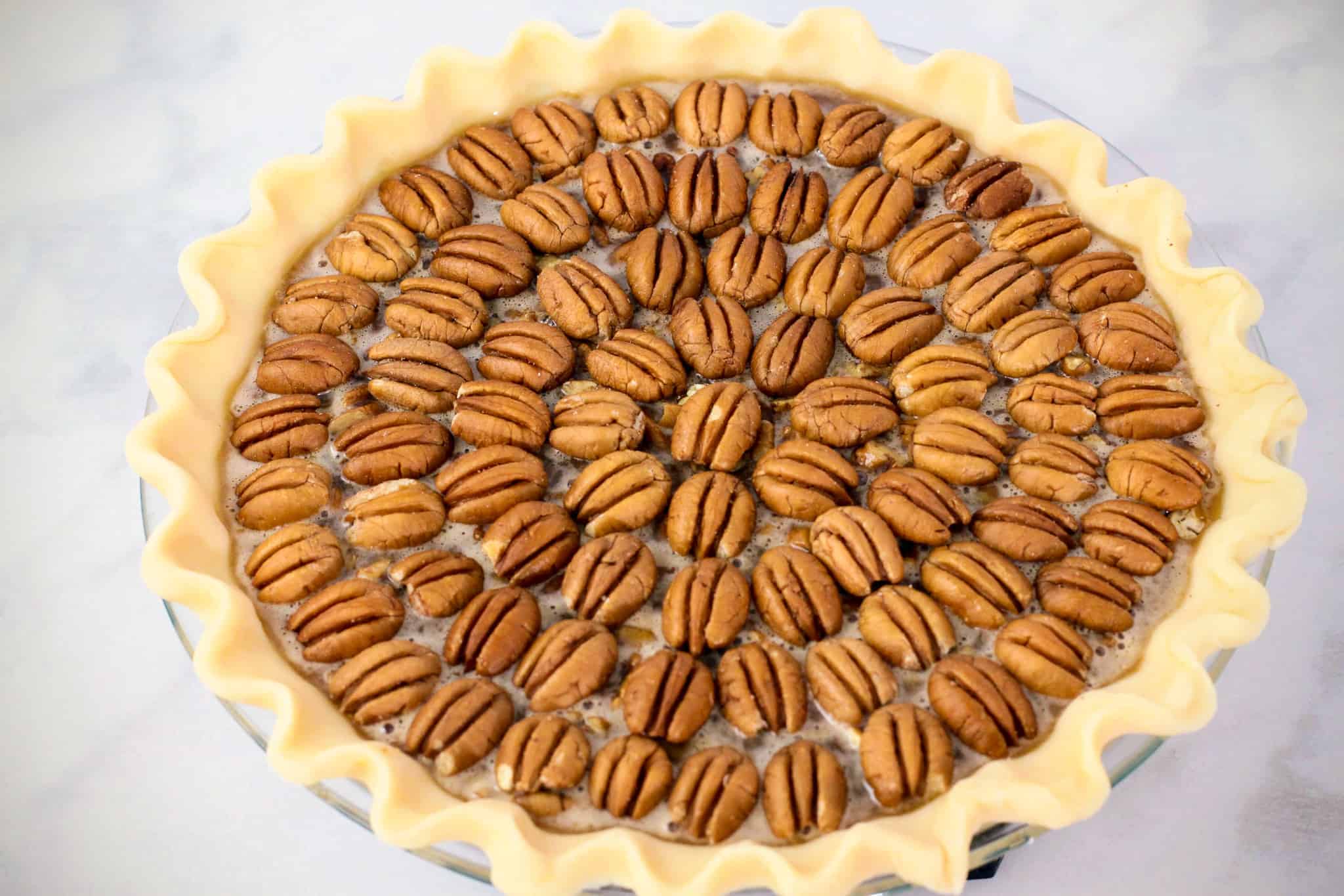 Side angle view of a prepared pecan pie with the pecan topping arranged in a concentric circle pattern.