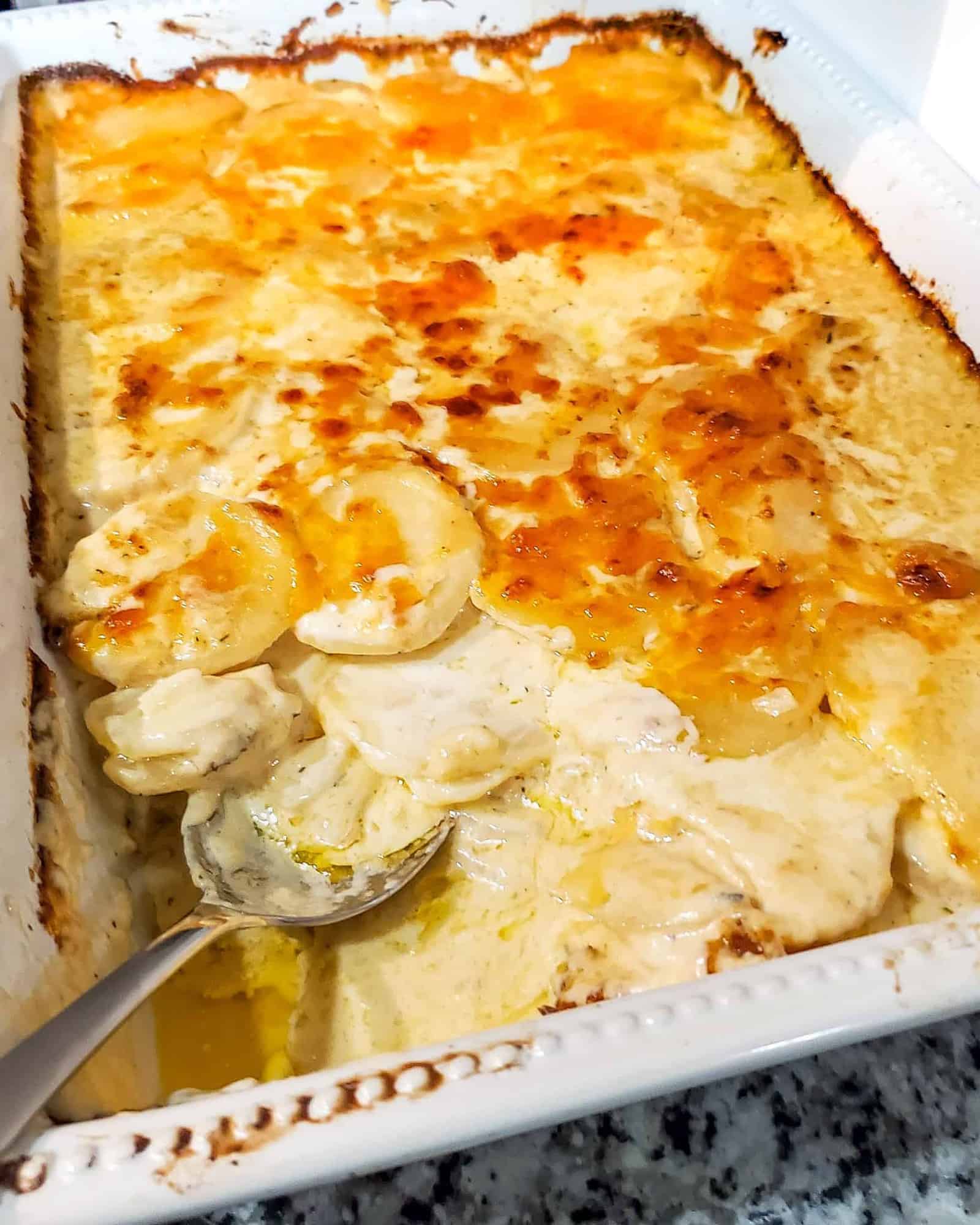 Scalloped Potatoes shown in a baking dish with golden brown cheese on top and layers of creamy, cheesy potatoes.