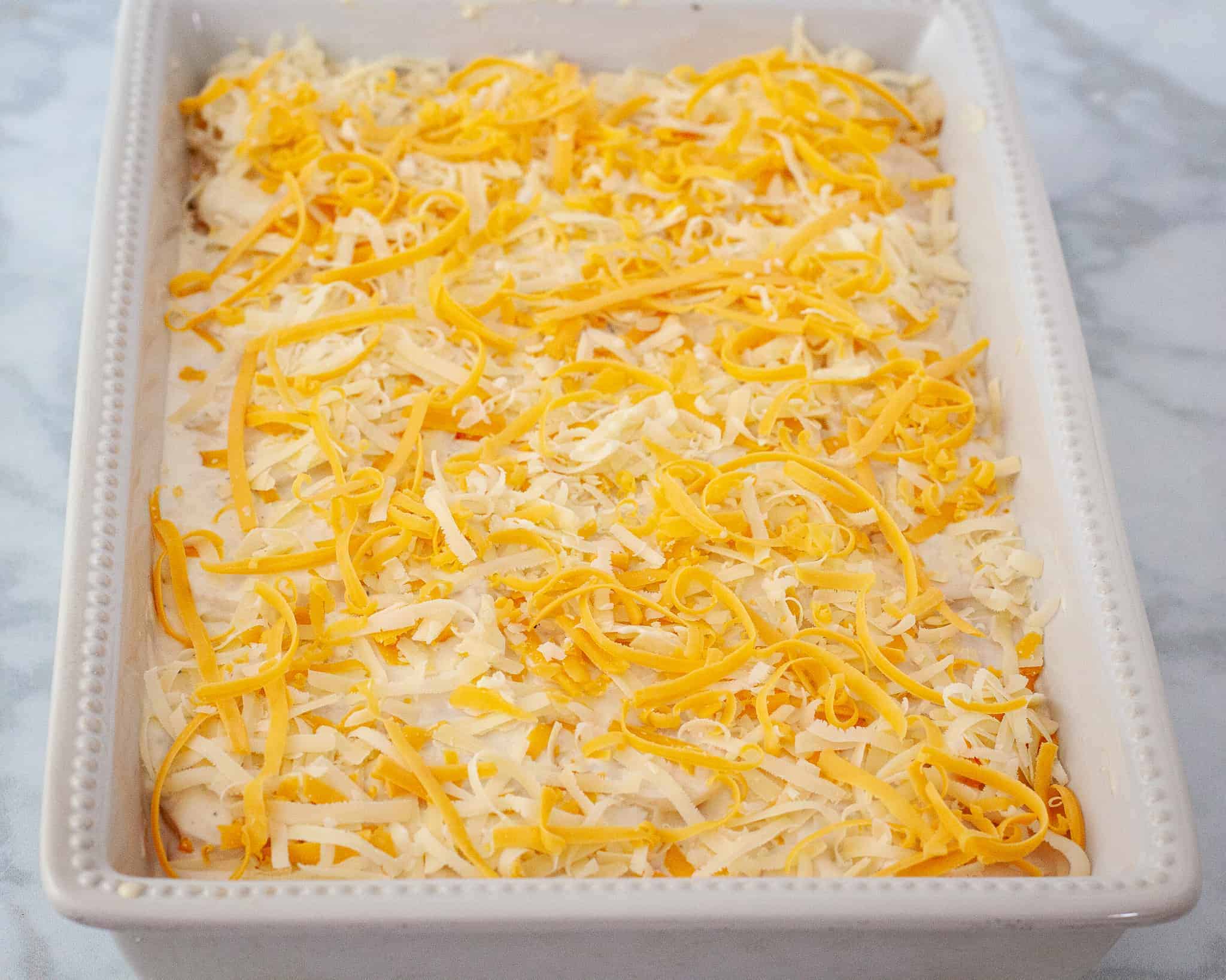 The assembled scalloped potatoes are shown in a baking dish topped with shredded cheese.