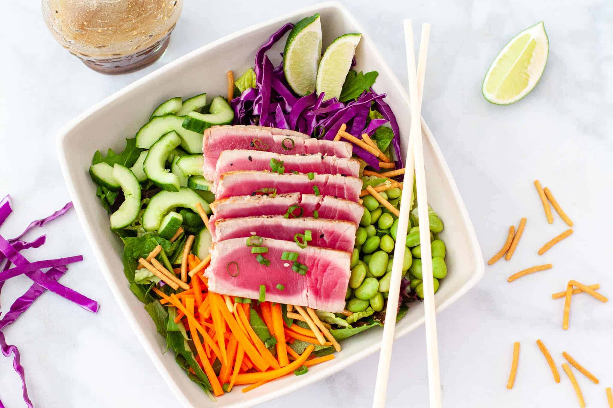 Overhead image of a bowl of salad topped with sliced seared tuna.