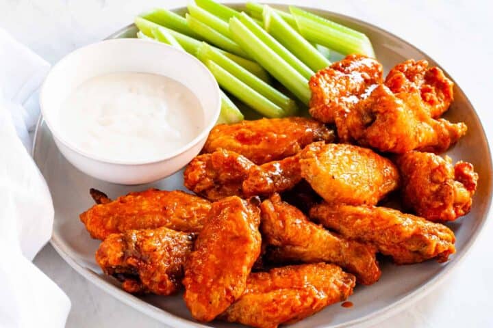 A platter of Buffalo chicken wings served with celery and dipping sauce.