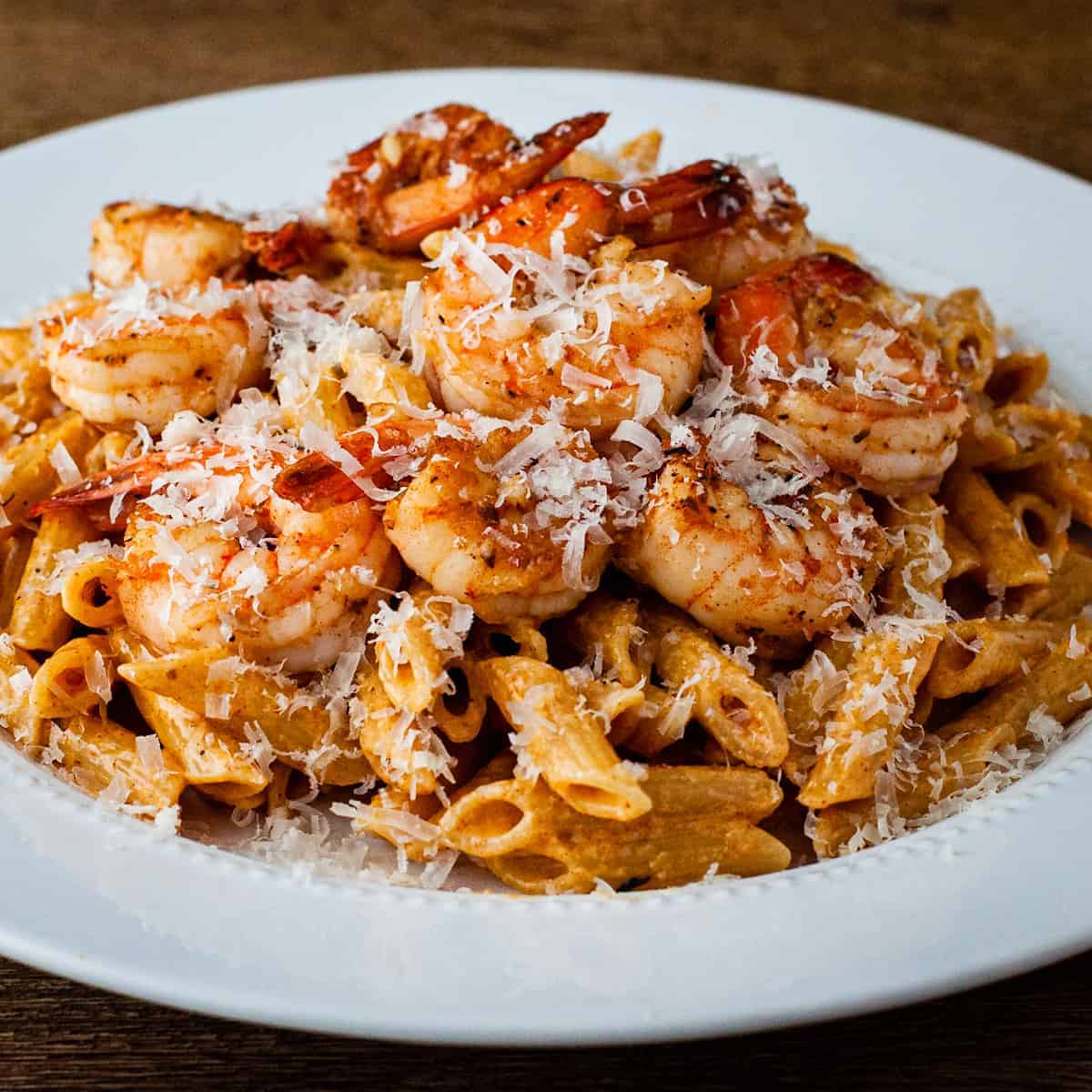 Side angle view of a large plate of creamy Cajun pasta topped with shrimp and grated parmesan cheese.