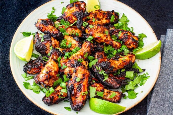 Grilled Chili Lime Chicken Wings served on a platter with lime wedges and scallions. 