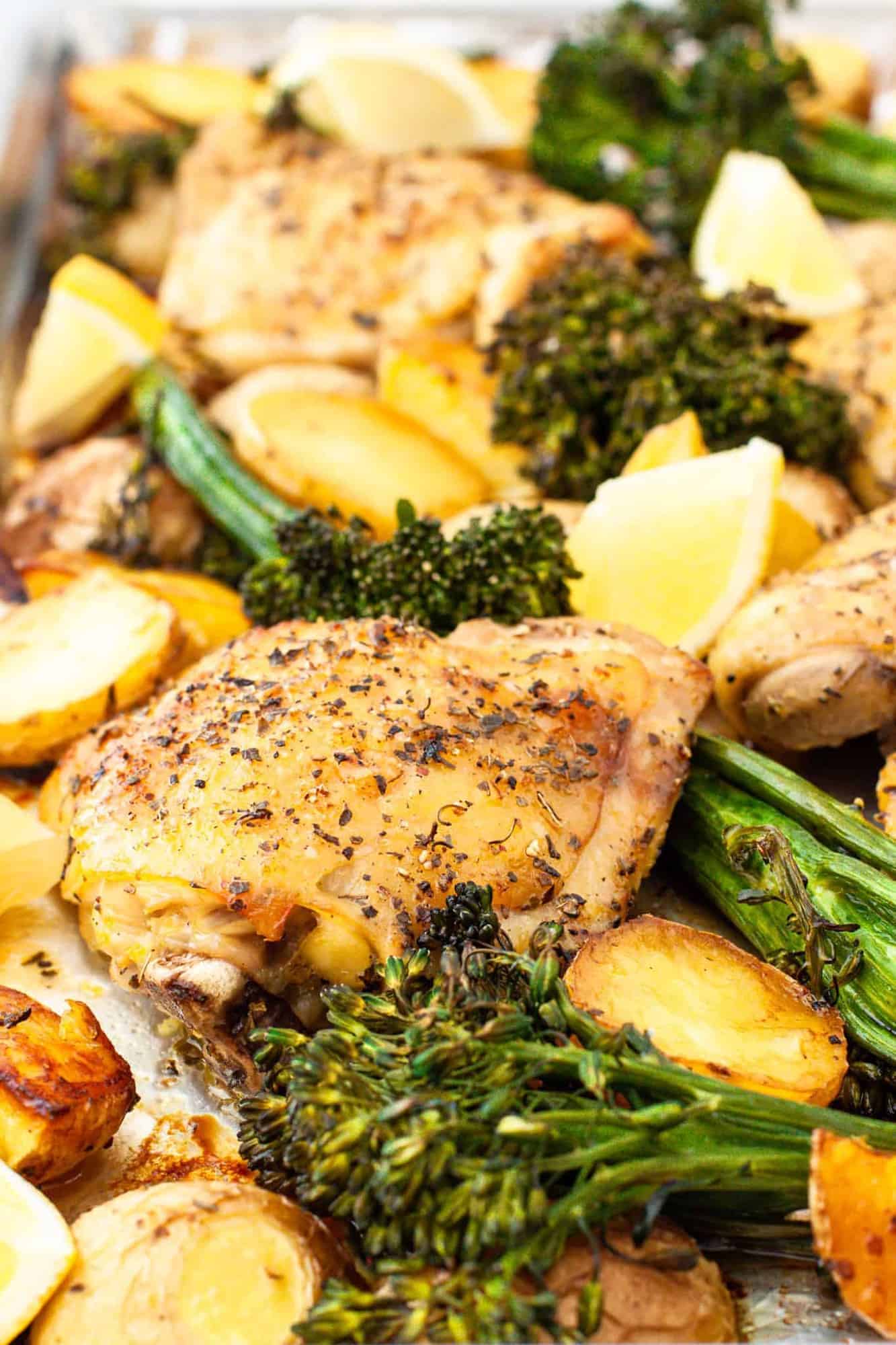 Close up of a roasted chicken thigh and broccoli on a sheet pan.