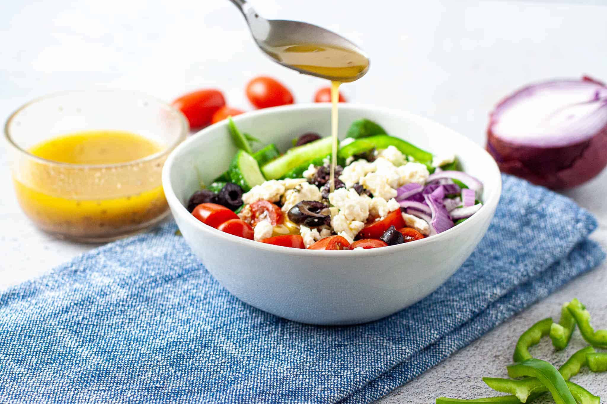 A bowl of salad on a counter with salad dressing being drizzled on top.