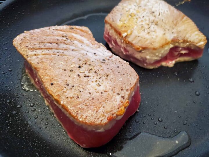Tuna shown in a pan, seared on one side and cooking on the other side.