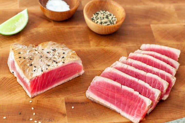 Slicing seared tuna steaks on a wooden cutting board.