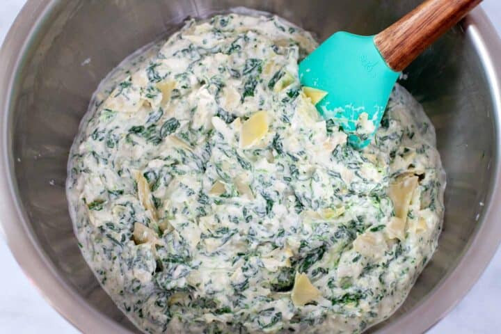 Mixing spinach artichoke dip ingredients in a mixing bowl.