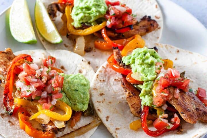 A plate of prepared chicken fajitas topped with guacamole and pico de gallo.