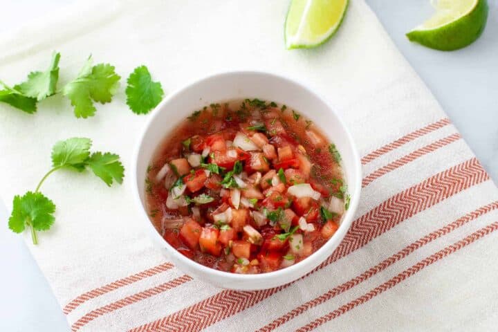 Pico de gallo salsa served in a bowl pictured with lime wedges and cilantro