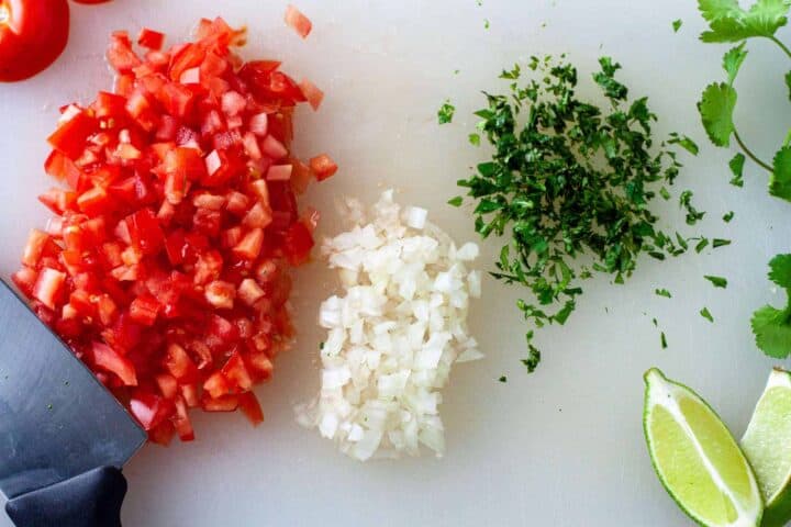 Fresh diced tomatoes and onions with cilantro and lime wedges on a cutting board.