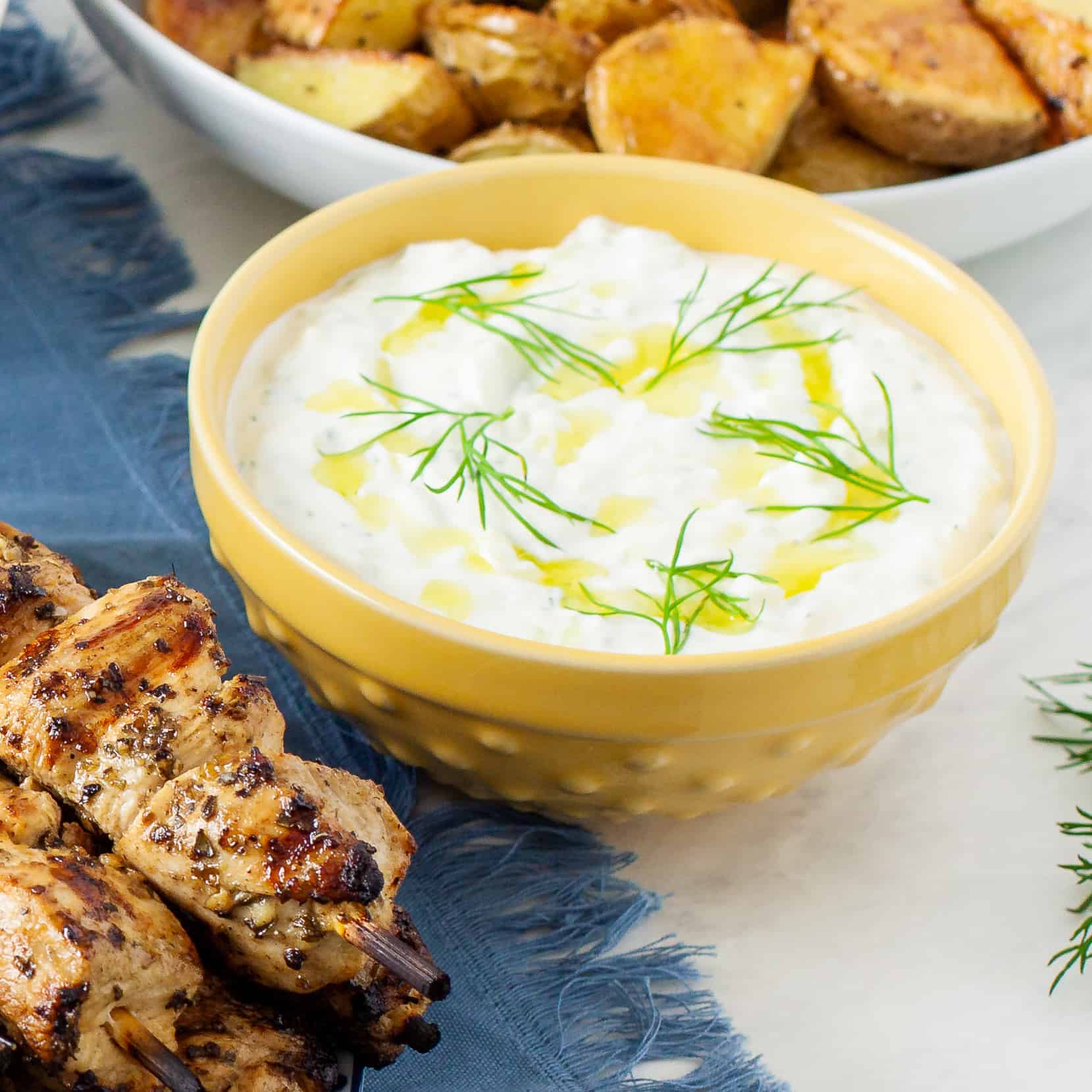 Tzatziki sauce in a yellow bowl topped with olive oil and fresh dill.