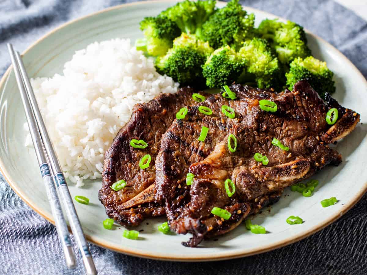 A plate of grilled short ribs served with steamed rice and broccoli.