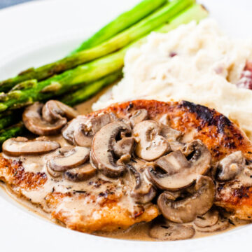 Close up image of a serving of chicken marsala showing golden brown chicken smothered in a creamy mushroom marsala sauce.