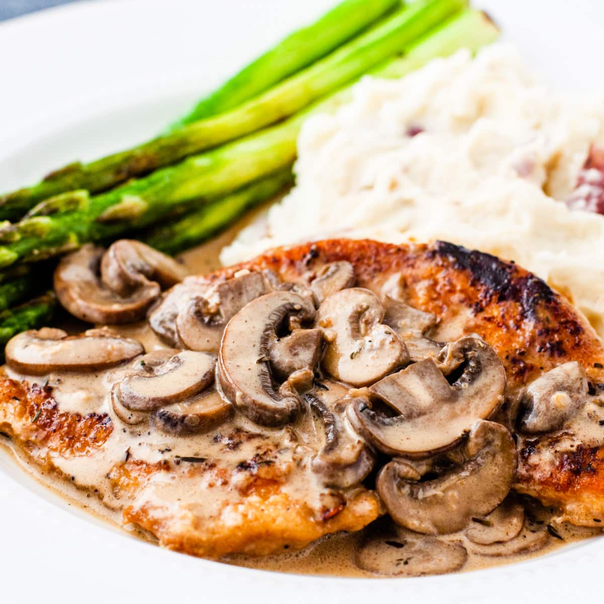 Close up image of a serving of chicken marsala showing golden brown chicken smothered in a creamy mushroom marsala sauce.