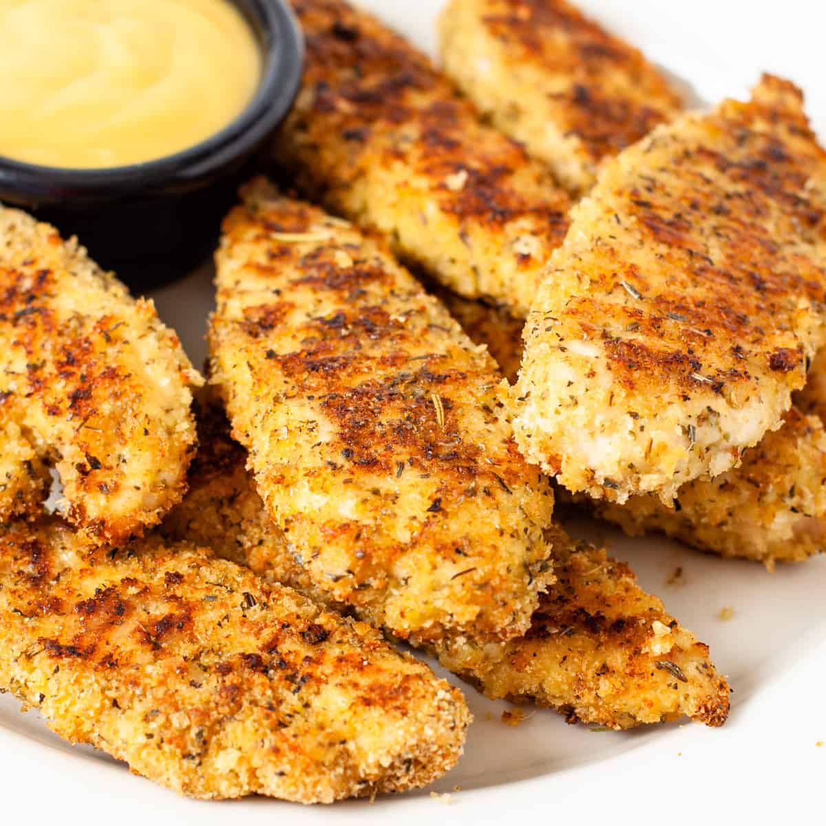 A plate of oven baked chicken fingers served with honey mustard.