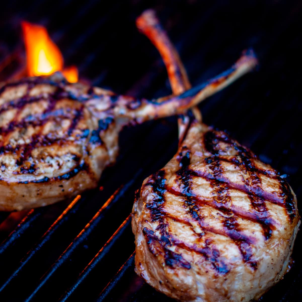 Pork chops shown being grilled over hot flames.