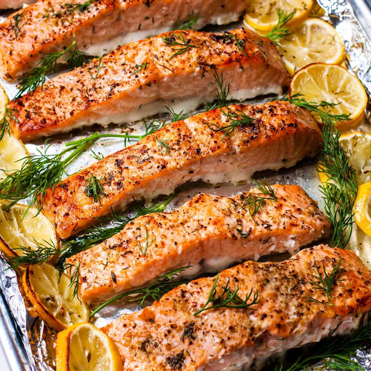 Side angle view of the lemon dill salmon surrounded by roasted lemon slices and fresh dill.