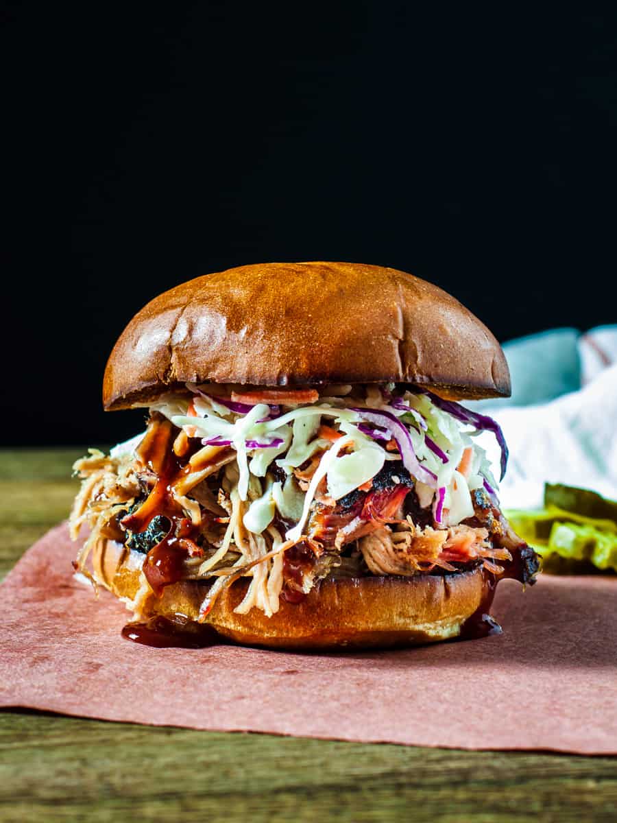 Side view of a pulled pork sandwich topped with slaw and BBQ sauce.