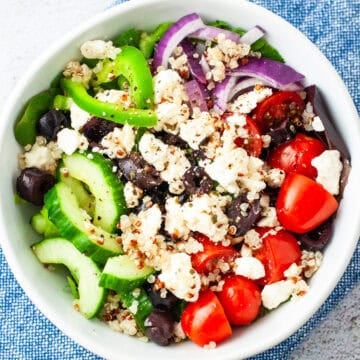 A Greek salad with quinoa and kale served in a small bowl.