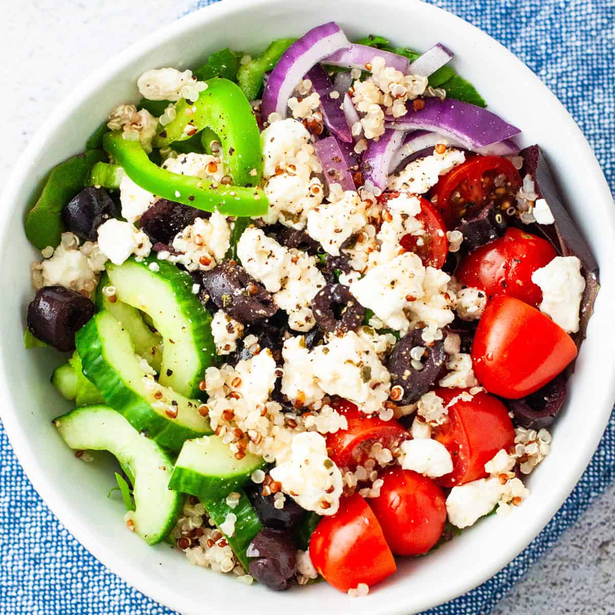 A Greek salad with quinoa and kale served in a small bowl.