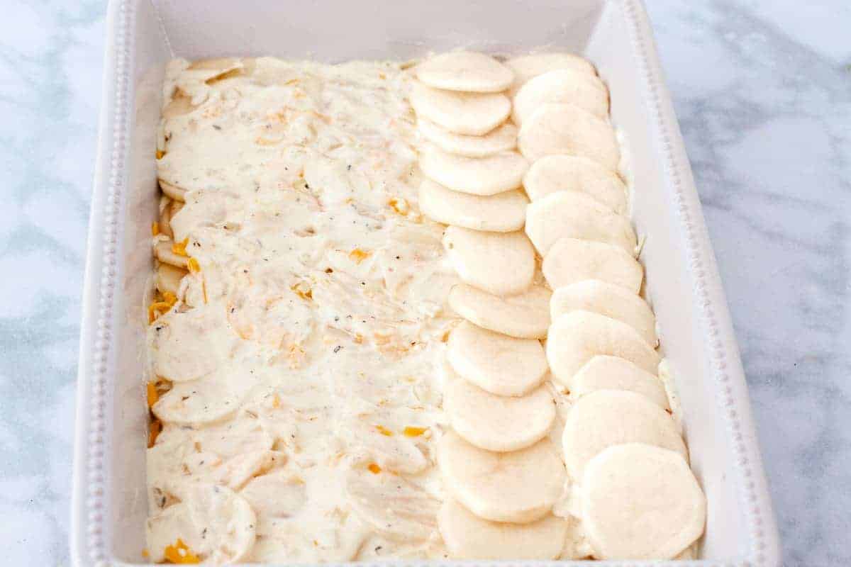 The scalloped potatoes are shown being assembled in a baking dish with layers of sauce, cheese, and potatoes