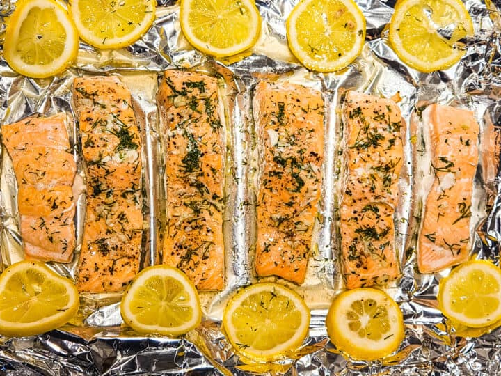 Salmon baked with lemon and fresh dill shown on a foil lined sheet pan.