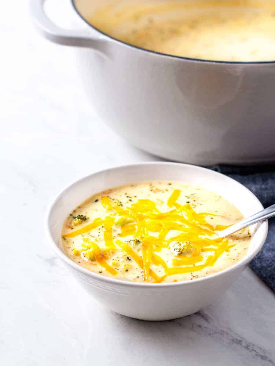 A bowl of broccoli cheese soup topped with grated cheddar cheese.