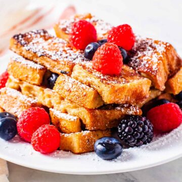 French toast sticks served on a plate topped with powdered sugar and fresh berries