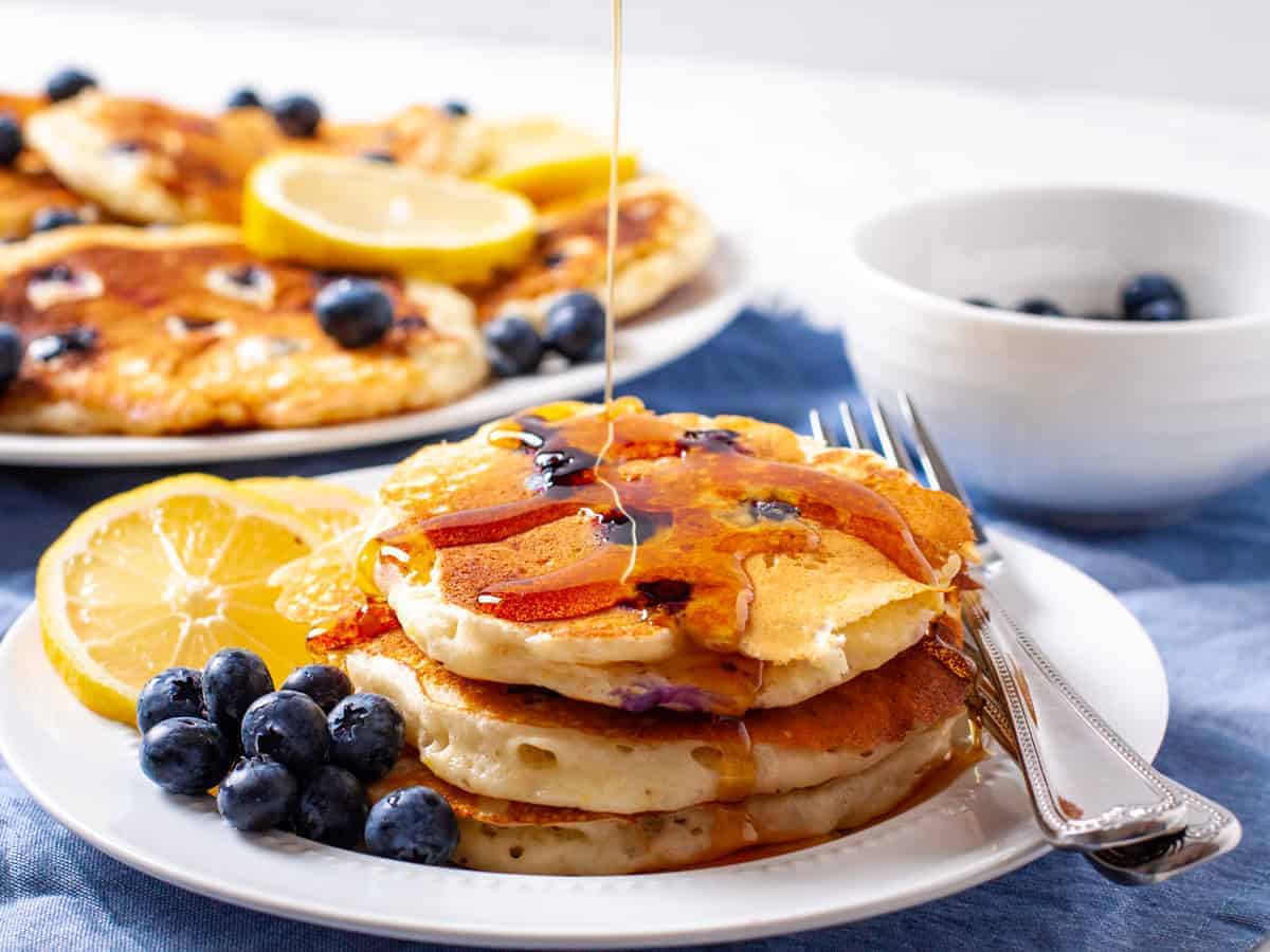 A plate of fluffy lemon blueberry pancakes with a drizzle of warm maple syrup