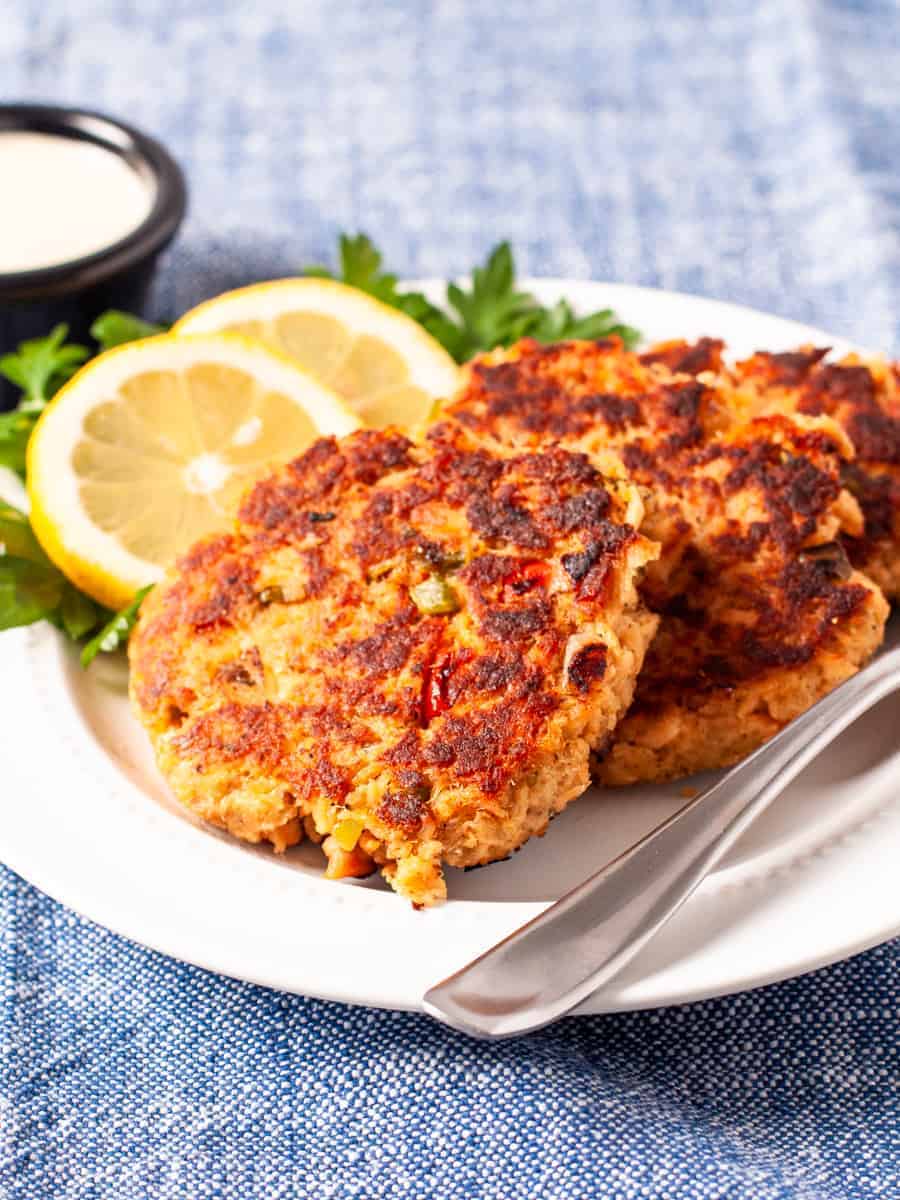 Golden brown salmon cakes served with dipping sauce and a garnish of fresh lemon slices and parsley.