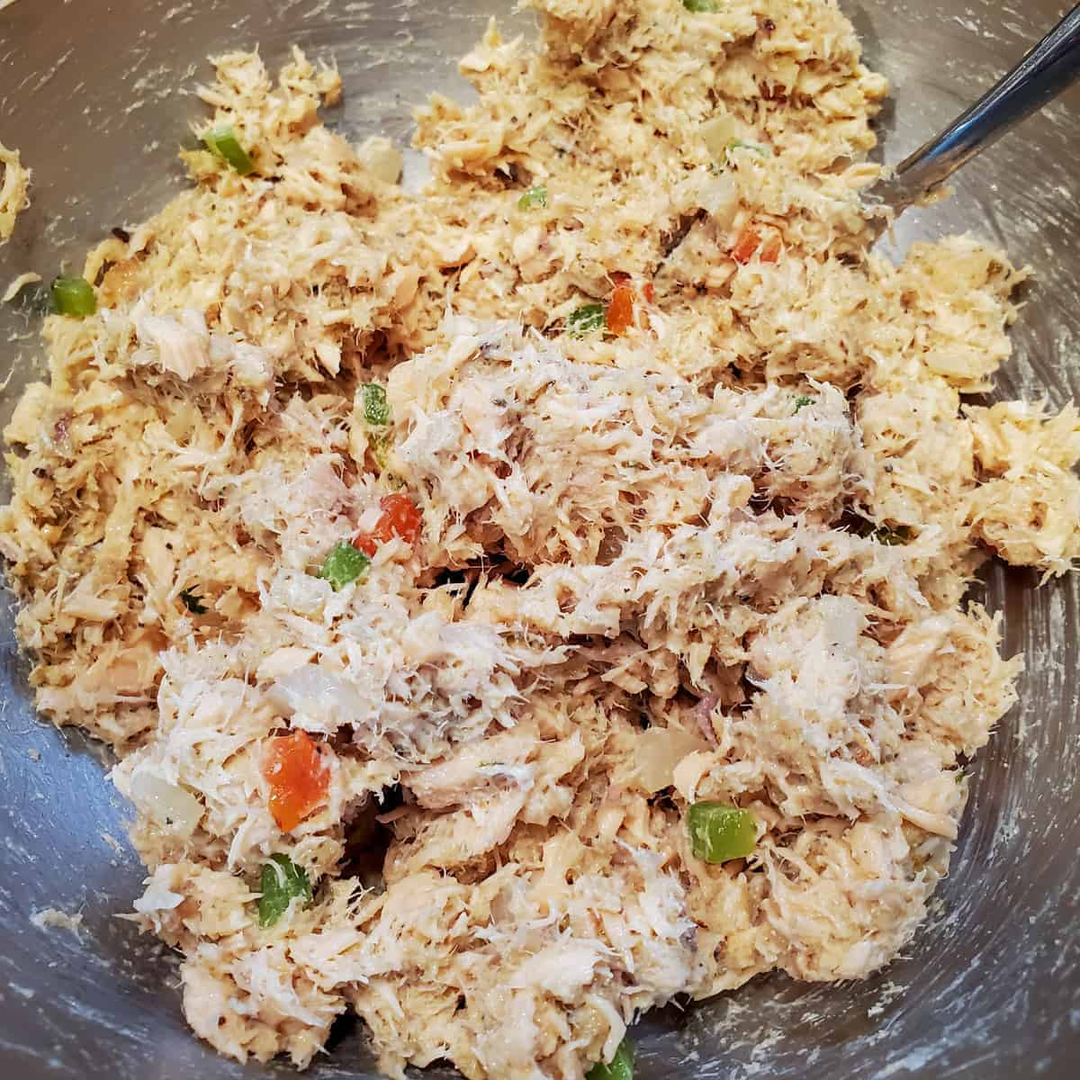 Mixture of cooked salmon, bread crumbs, mayonnaise, onion, and bell peppers in a mixing bowl. 