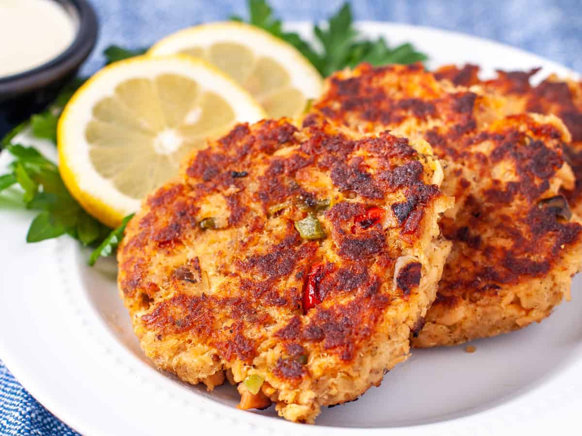 Close up shot of finished salmon cakes on a plate with fresh sliced lemon and parsley garnish.