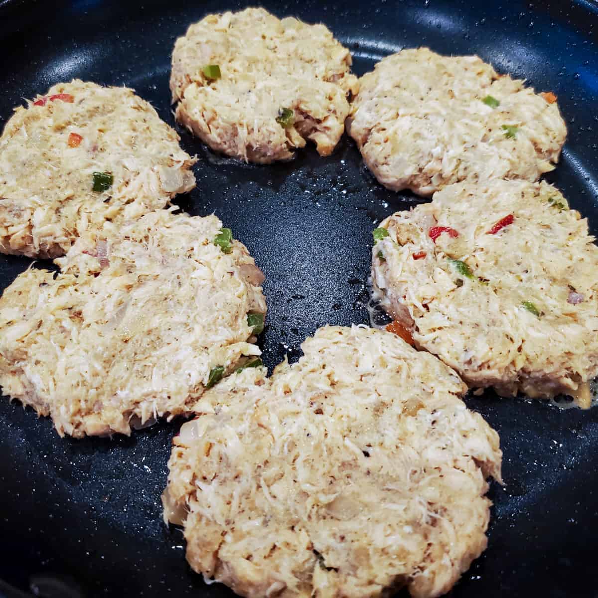 Salmon cake patties shown cooking in a large non-stick skillet