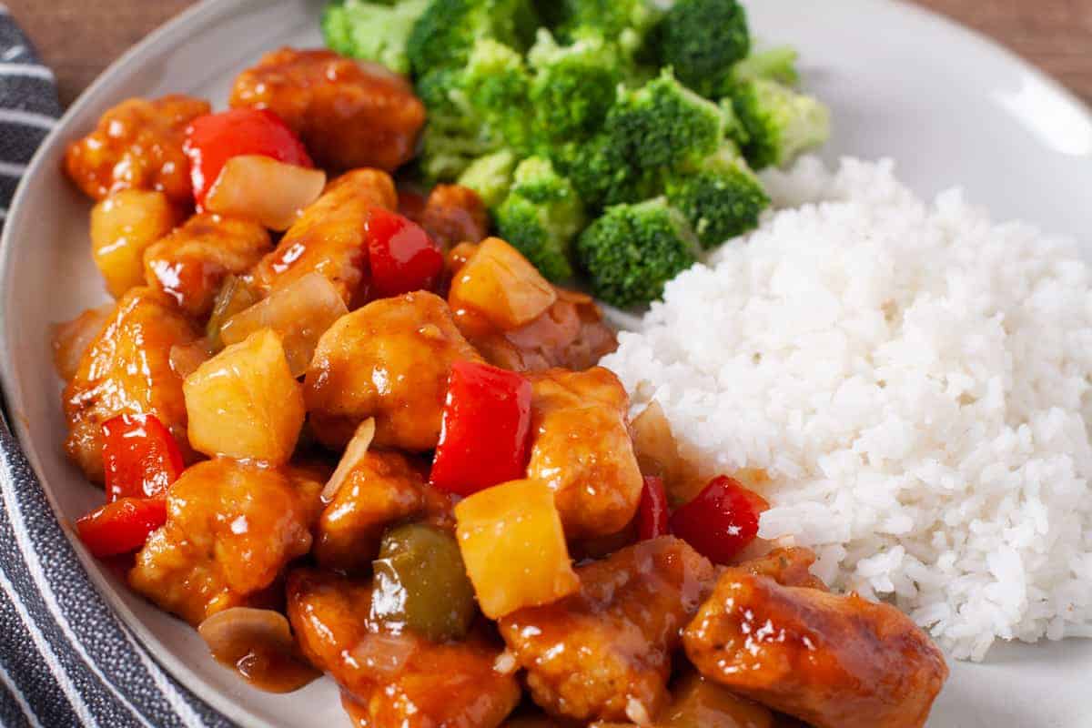 Finished plate of crispy golden brown sweet and sour chicken served with rice and broccoli.