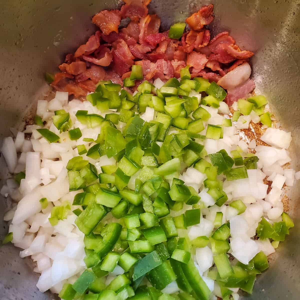 Cooked bacon and raw diced veggies shown in the Instant Pot ready to saute. 