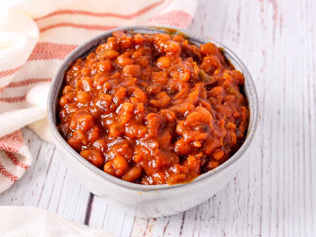 Image of the finished bowl of baked beans shown on a white wooden background.