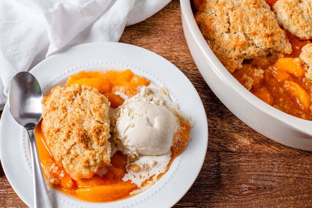 The finished cobbler is shown served on a plate with a scoop of vanilla ice cream.