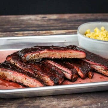 A platter of sliced ribs served with mac and cheese.