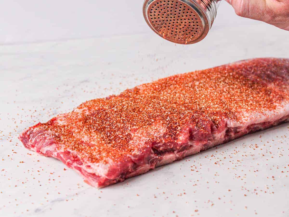 Pork spare ribs shown being seasoned with dry rub.