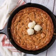 A chocolate chip cookie shown served in a cast iron skillet and topped with vanilla ice cream.